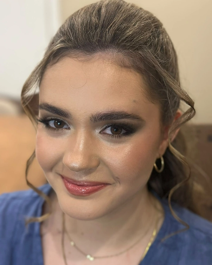 Clienta joven con ahumado gris, piel con brillo y labios rosados; sonríe.